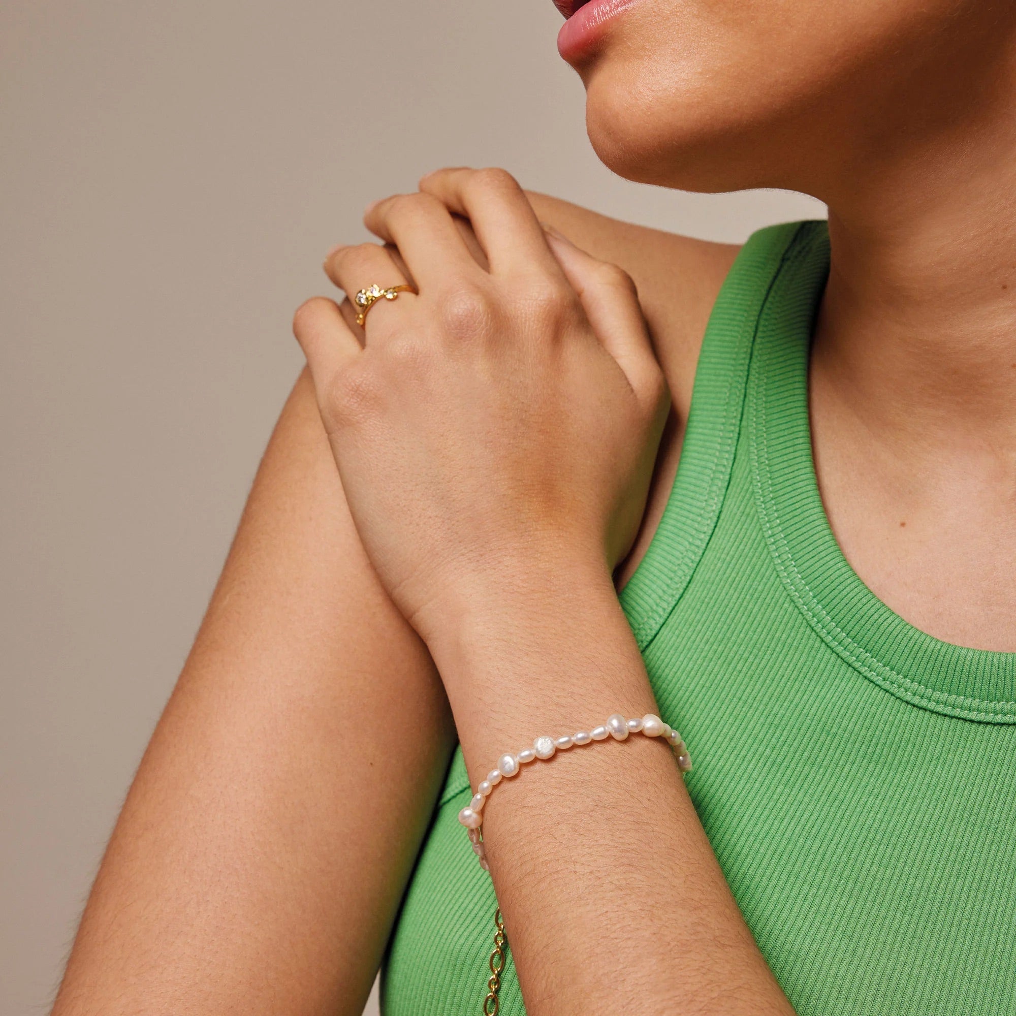Close-up of a person wearing a gold ring and pearl bracelet on a neutral background