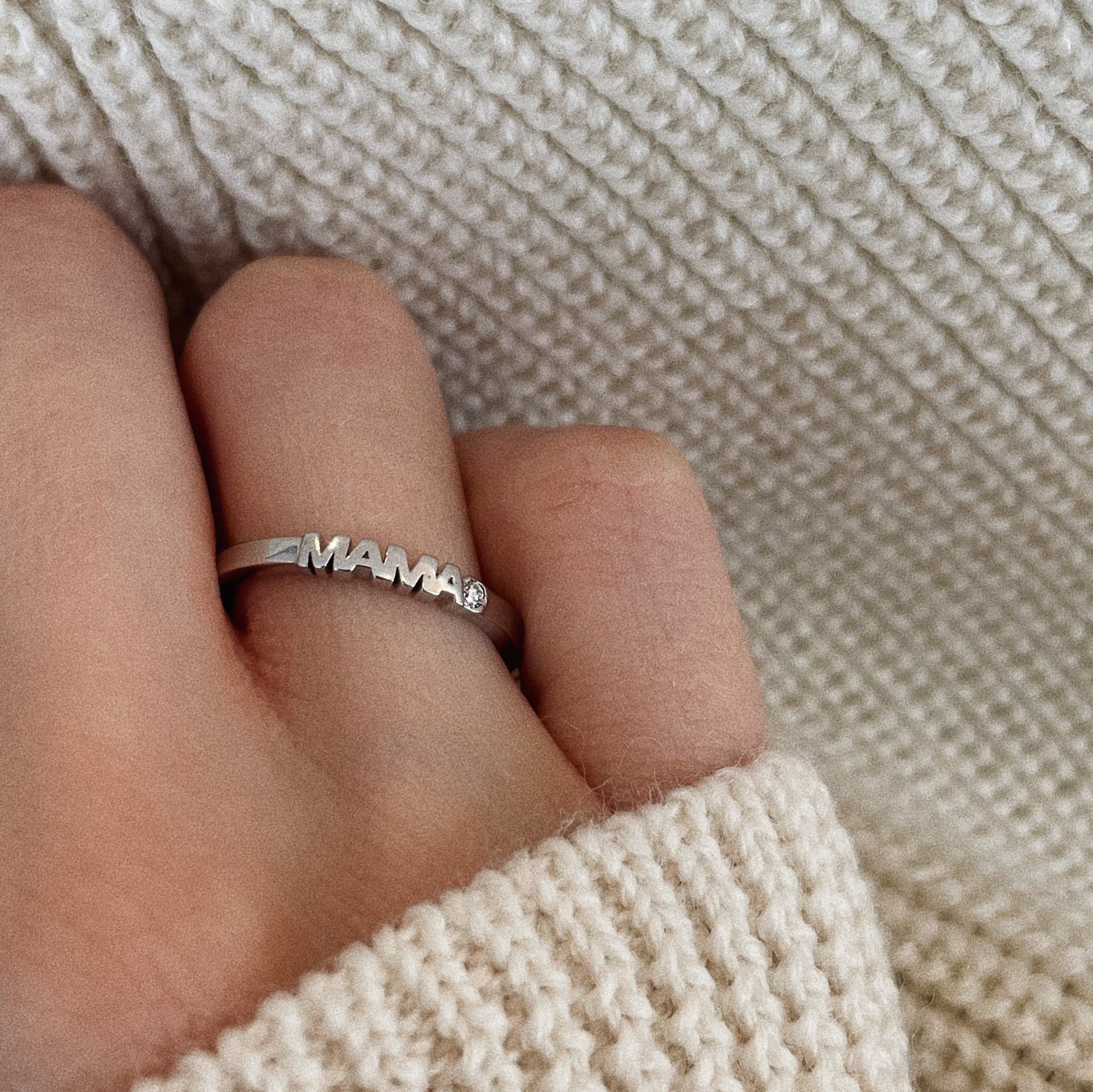 Hand wearing white gold ring with word Mama set with single diamond.