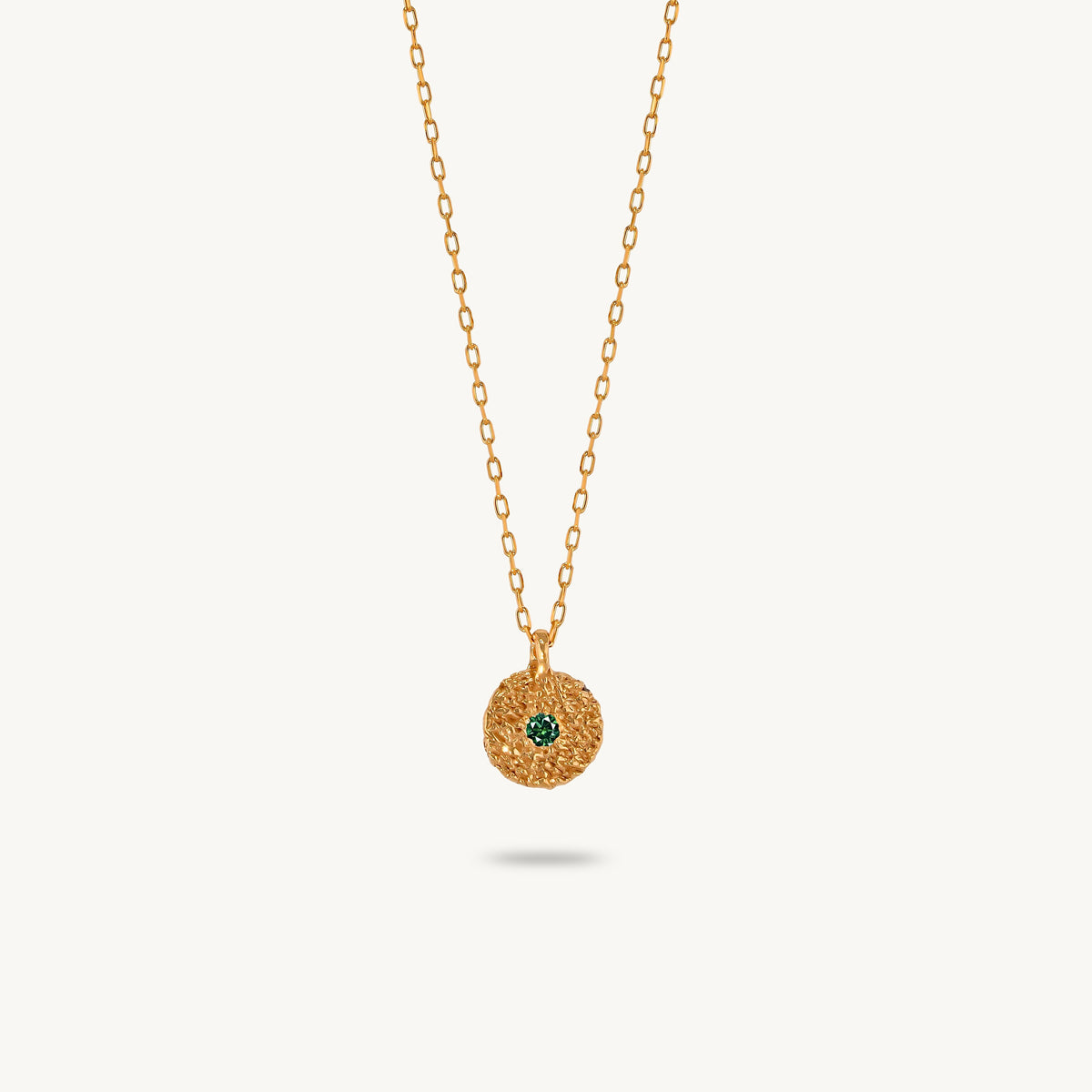 Gold-plated silver chain necklace featuring a round, textured disc pendant with a small emerald set in the center.