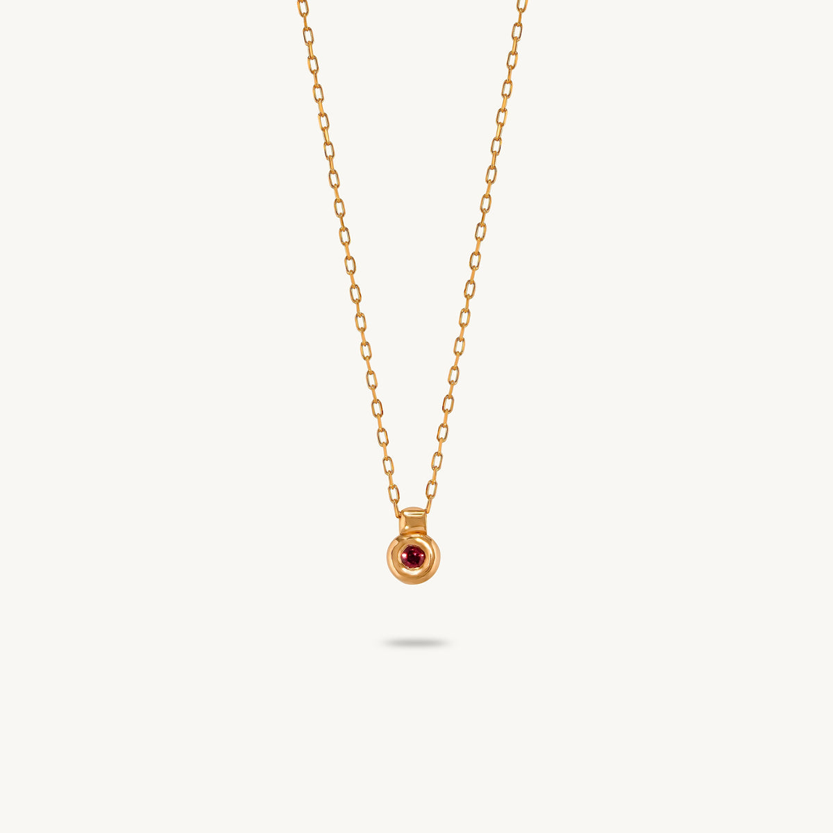A gold-plated silver pendant featuring a smooth, sculptural bezel framing a single central red sapphire.