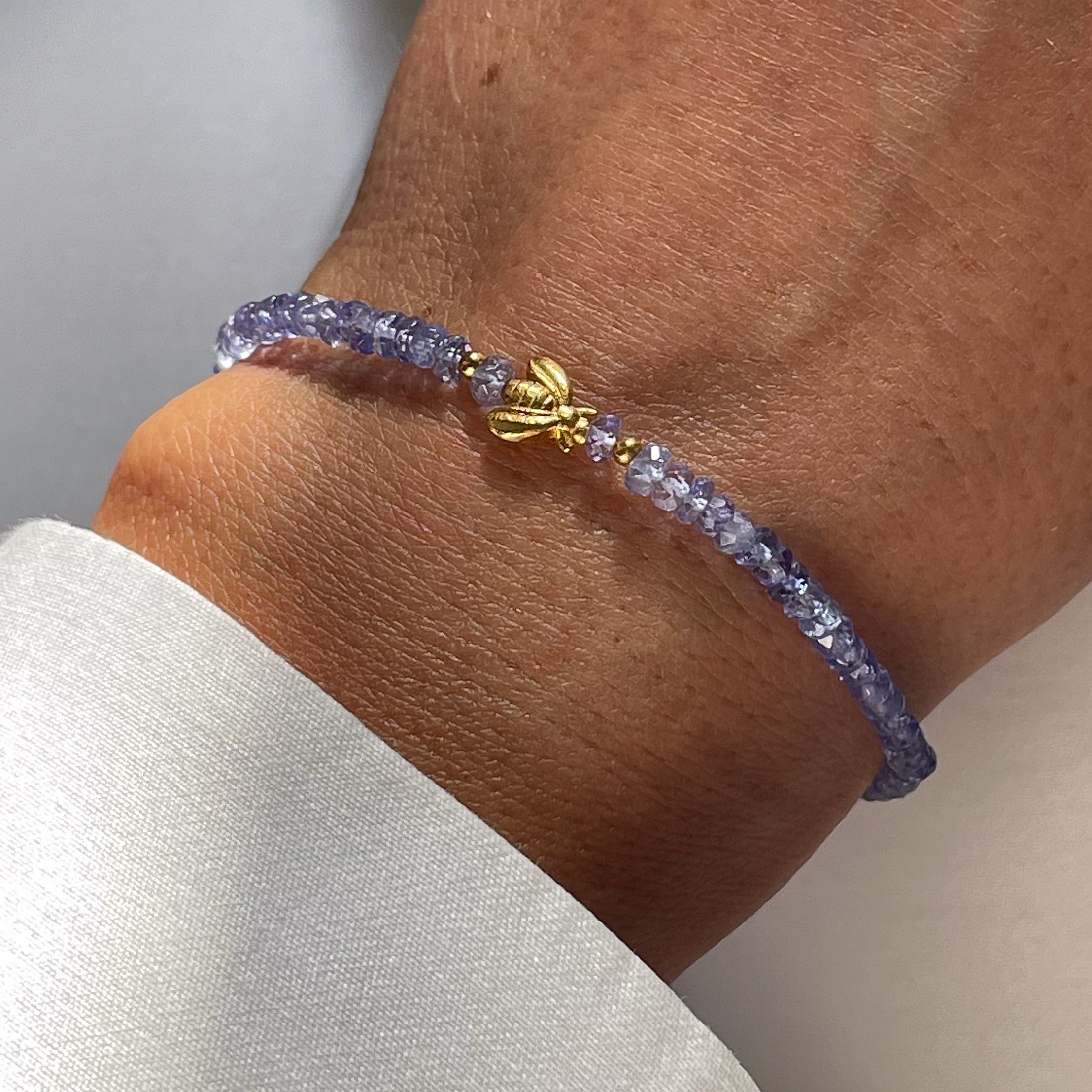A gold-plated silver bracelet with tanzanite beads and a gold-plated bee-shaped pendant on a person's wrist.