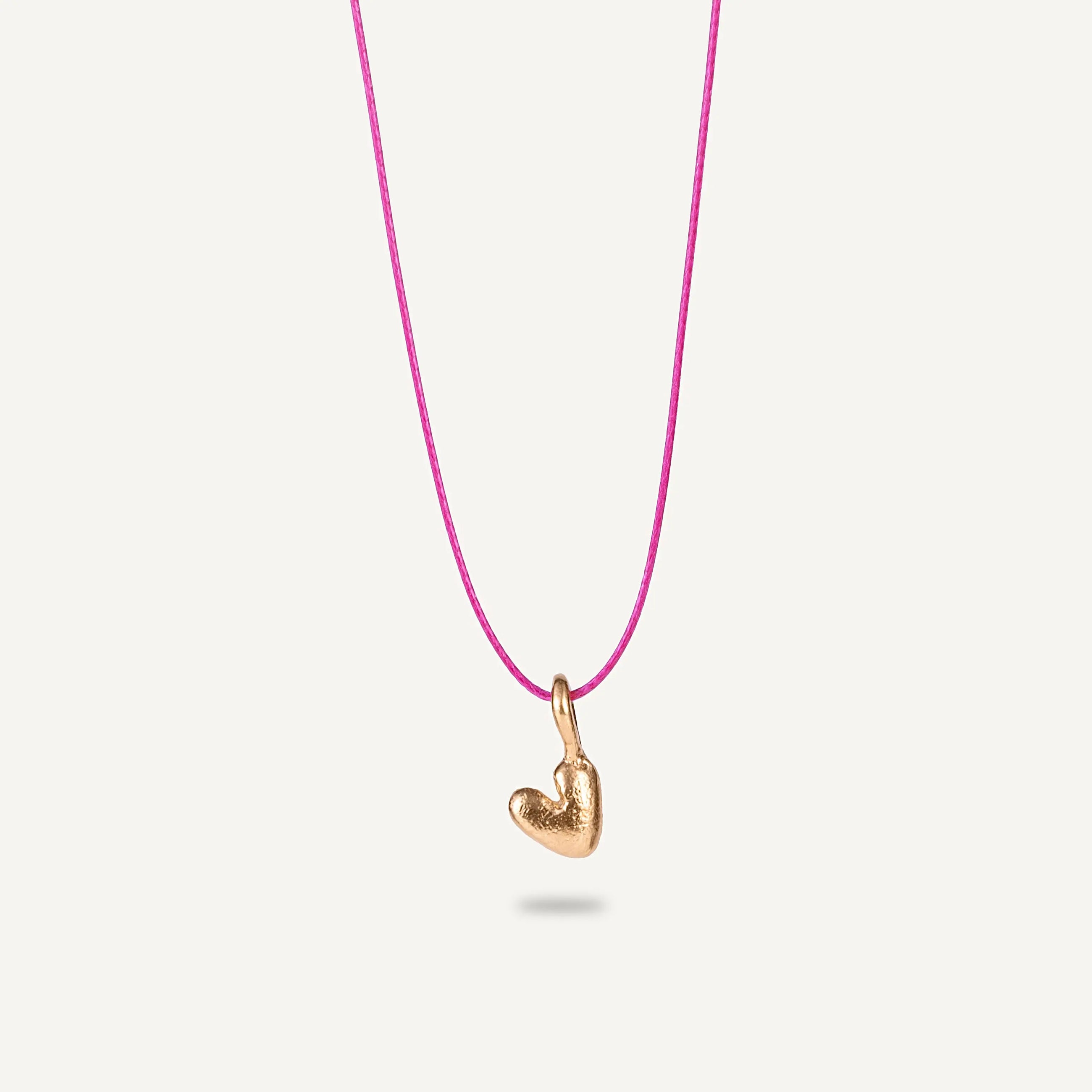 A gold plated silver necklace with a heart-shaped pendant on a pink string.