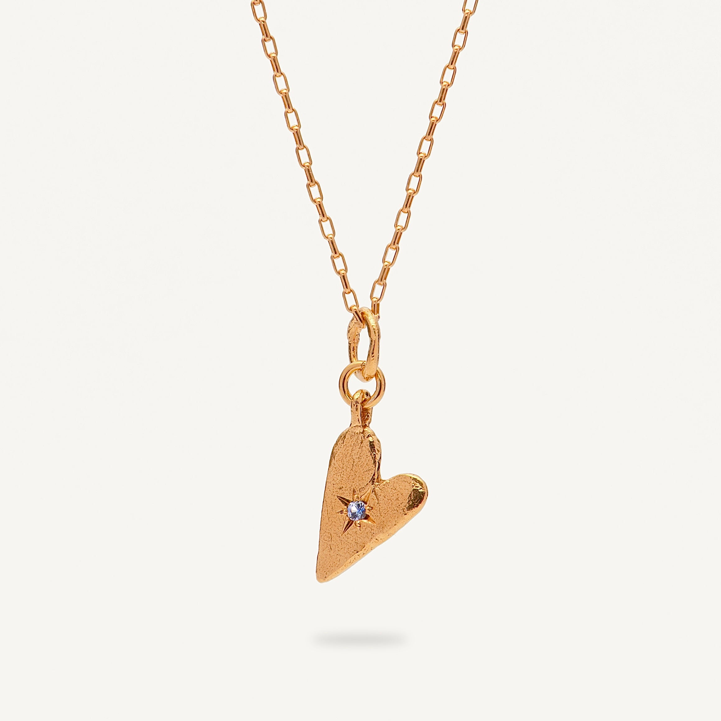 Gold heart-shaped pendant necklace with a small blue gemstone on a white background