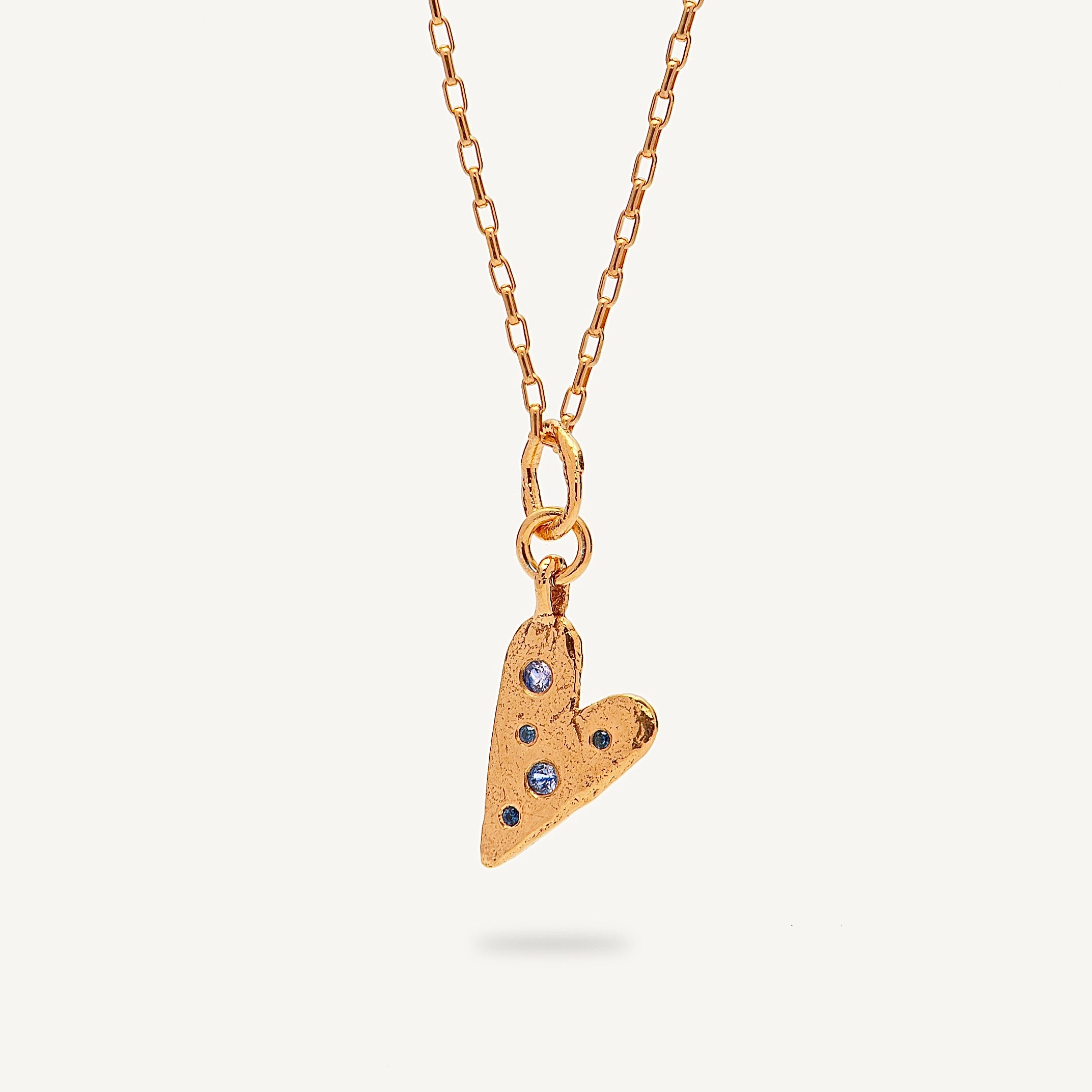 Gold heart-shaped pendant necklace with embedded stones on a light beige background