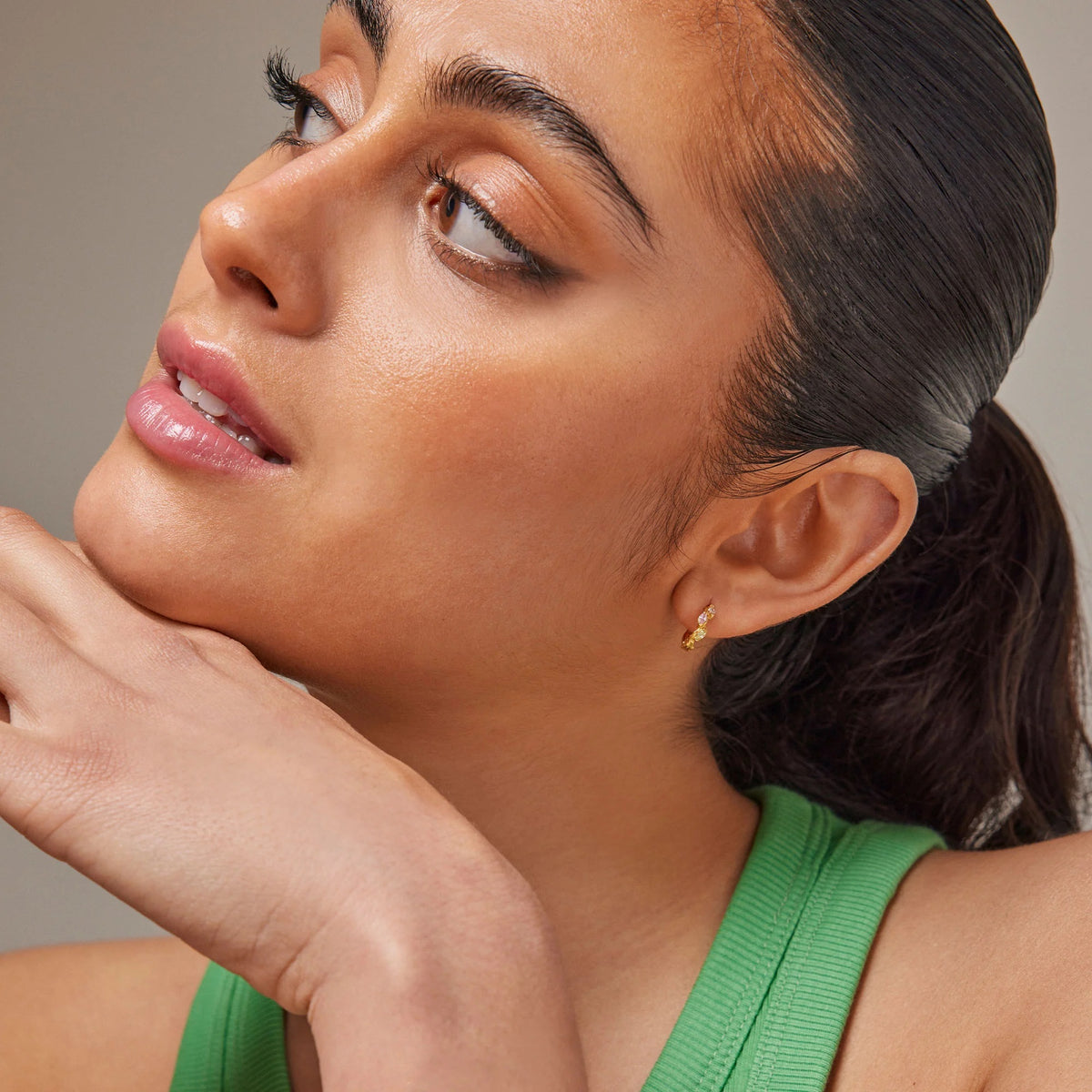Close-up of a woman with a green top and gold earring against a neutral background