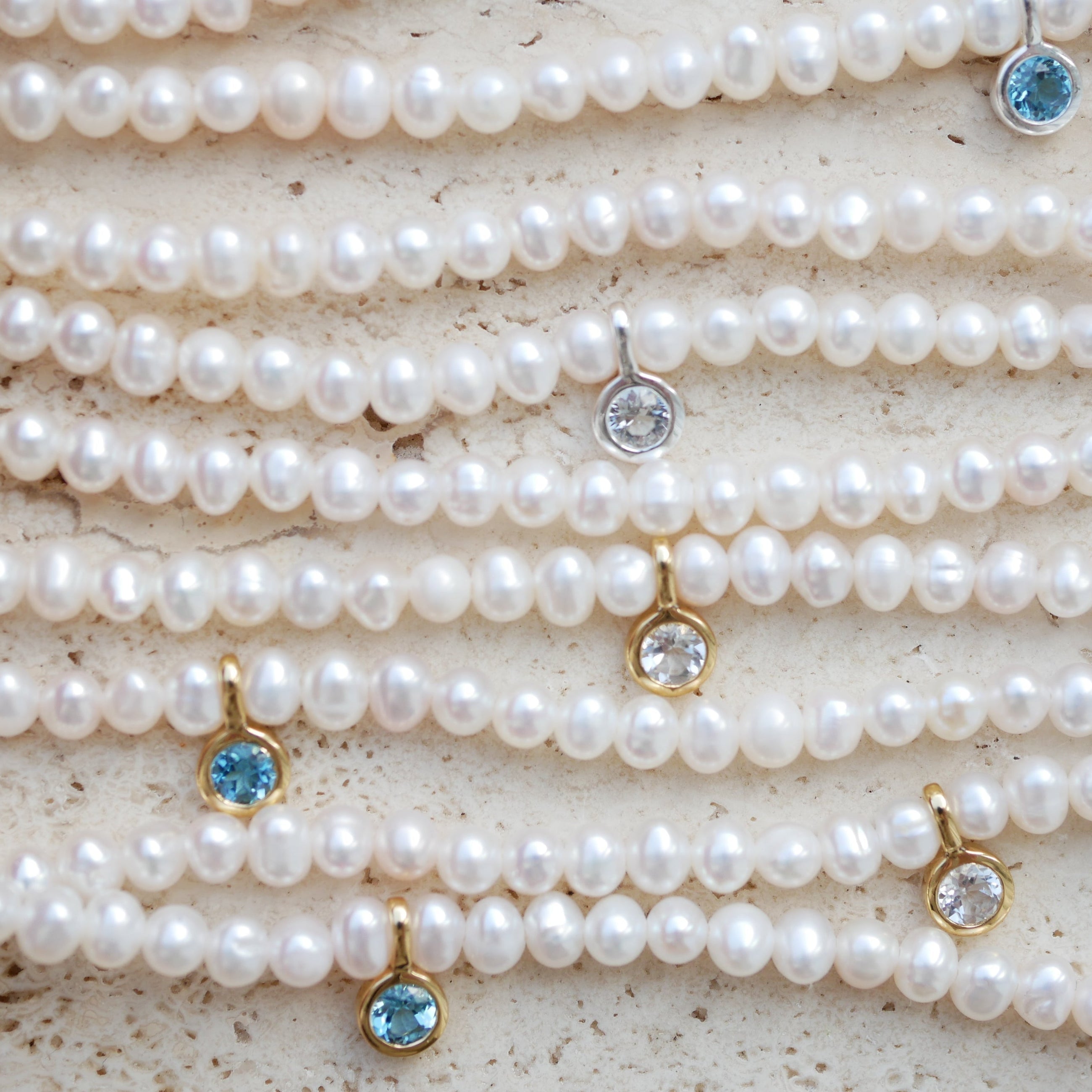 Pearl necklaces with topaz gemstone pendants on a textured surface