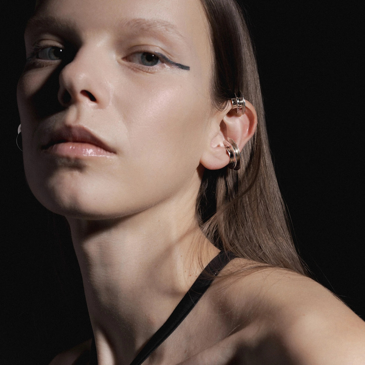 Close-up of a person wearing silver ear cuff earrings against a black background