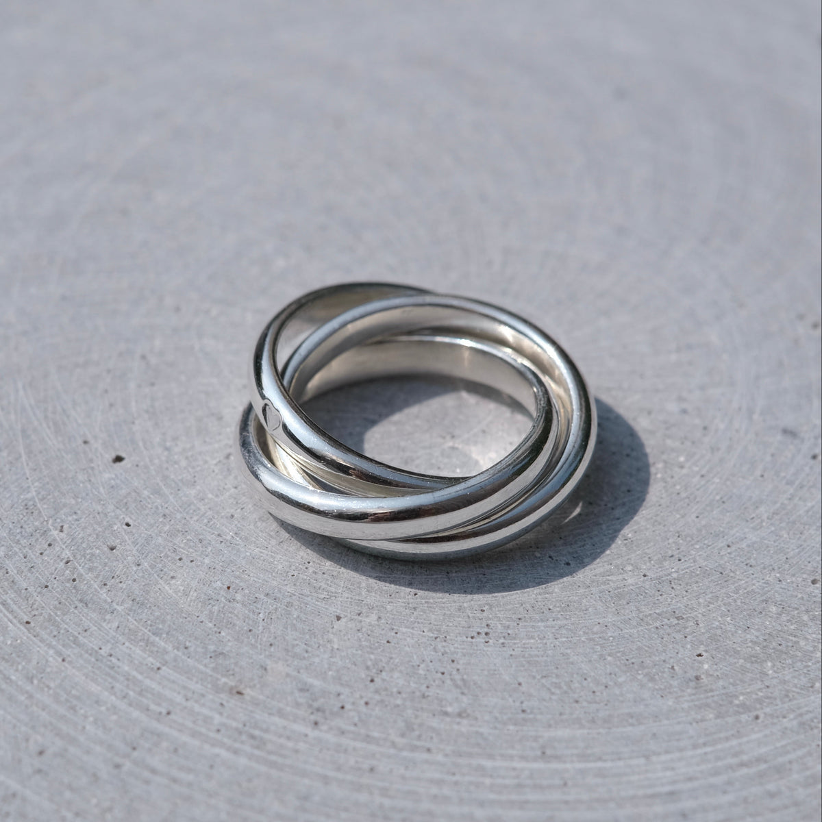 Three interlocked silver rings on a textured light gray surface.