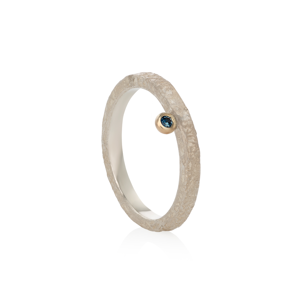A textured silver ring with a small bezel-set round blue gemstone, shown on a clean white background with a soft reflection.