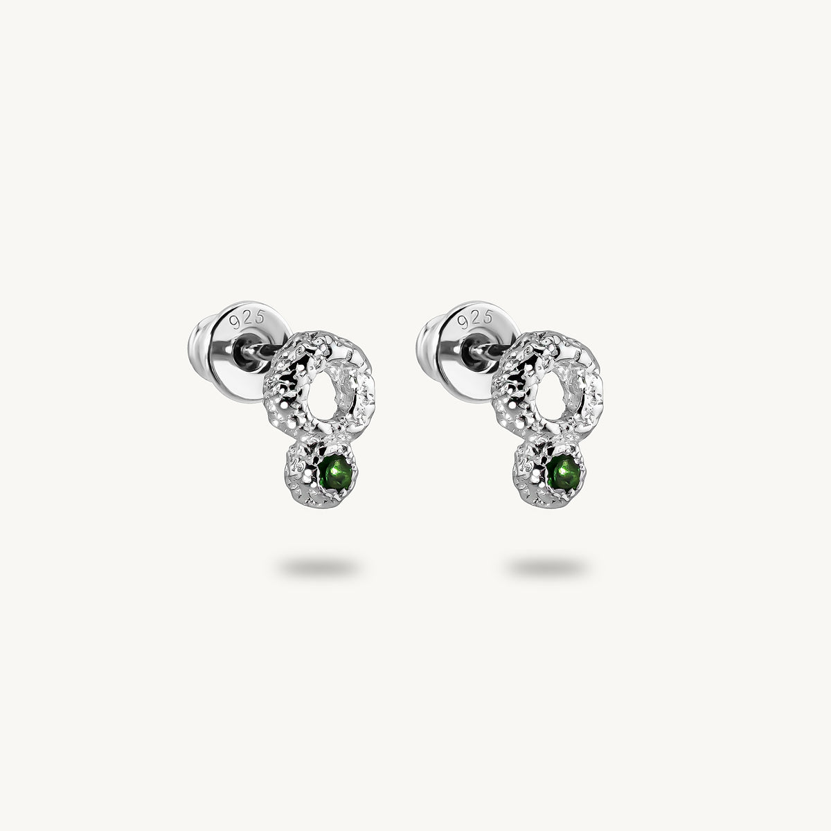 A pair of silver stud earrings, featuring a raw, artisanal textured surface and vibrant green emeralds.