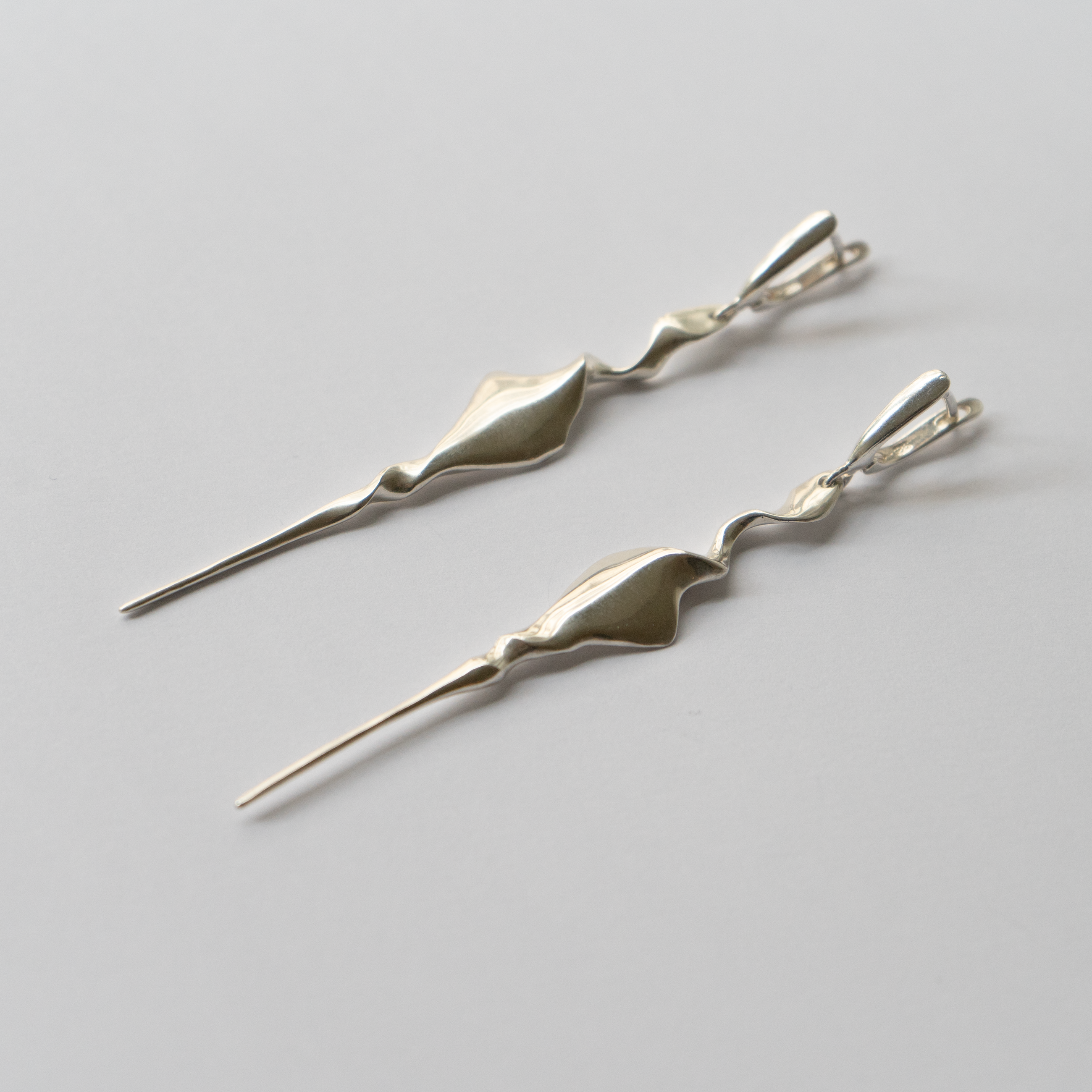 A pair of silver drop earrings with abstract, organic wavy shapes and fine wire-like ends, displayed on a clean light gray background.