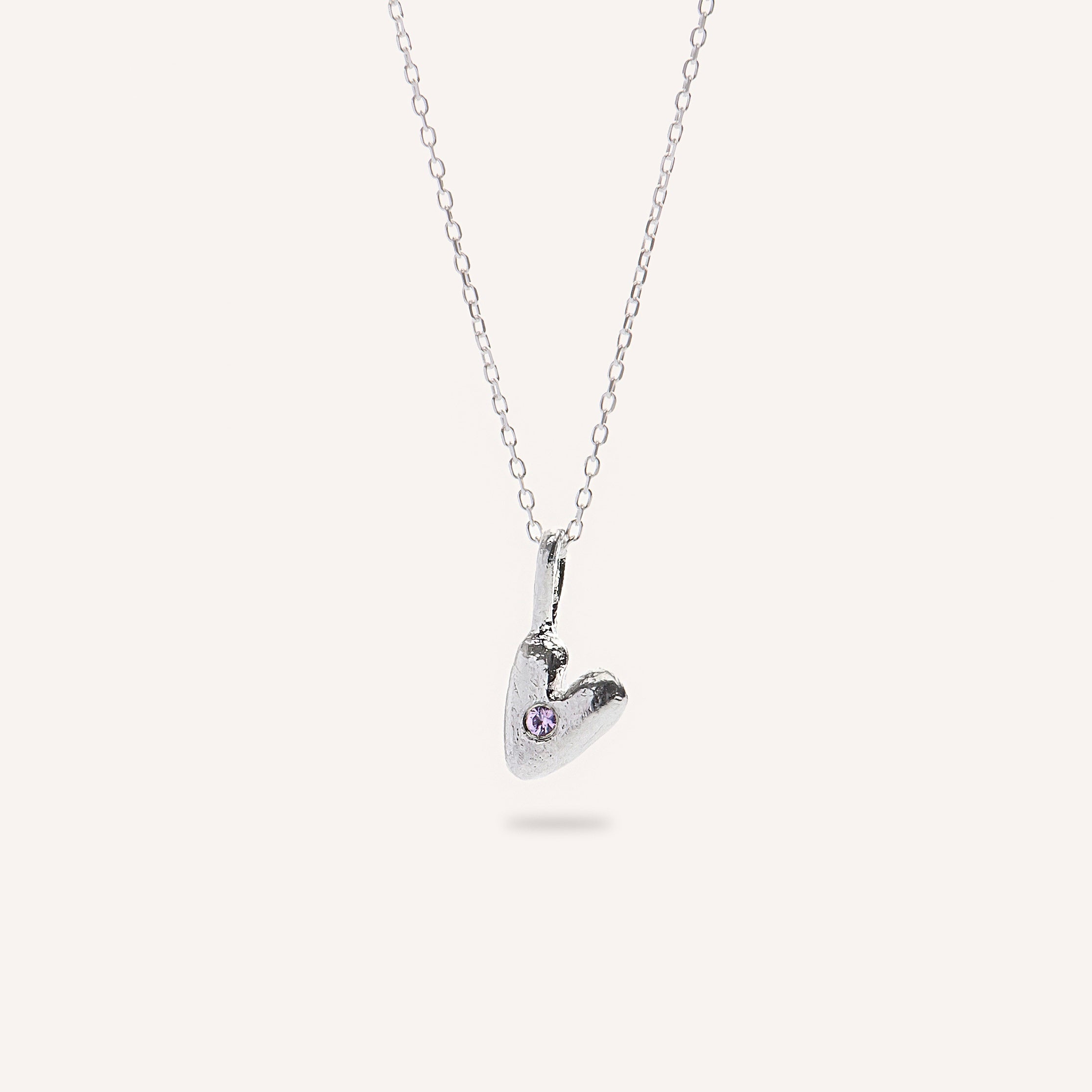 Heart-shaped silver pendant with a small gemstone on a white background
