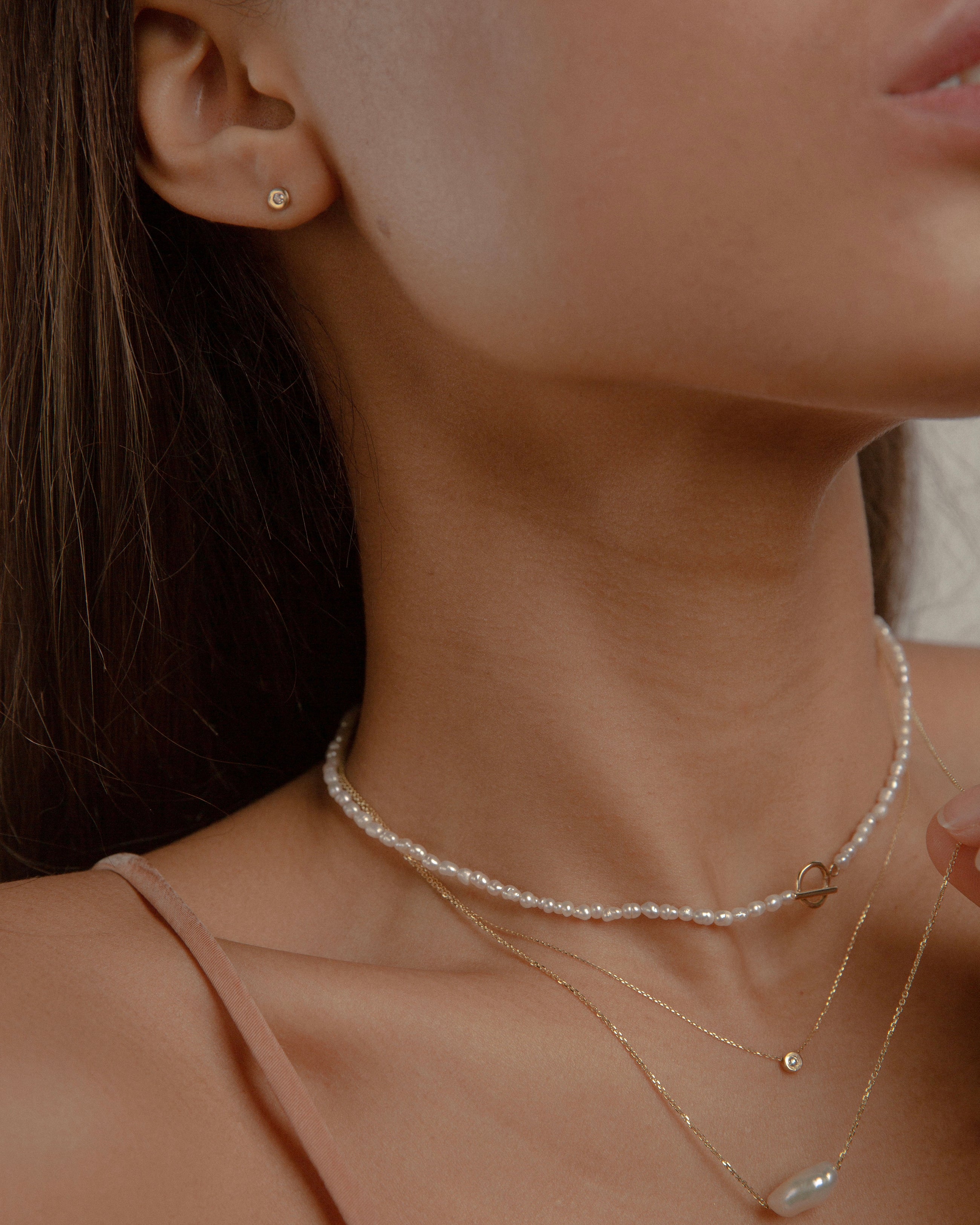 Woman wearing three minimal design yellow gold, pearls and diamonds necklaces.