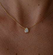 Gold necklace with a teardrop-shaped topaz pendant on a person's neck.