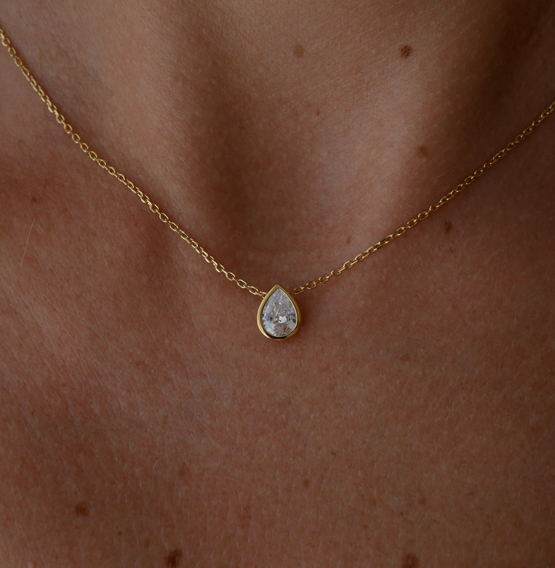 Gold necklace with a teardrop-shaped topaz pendant on a person's neck.