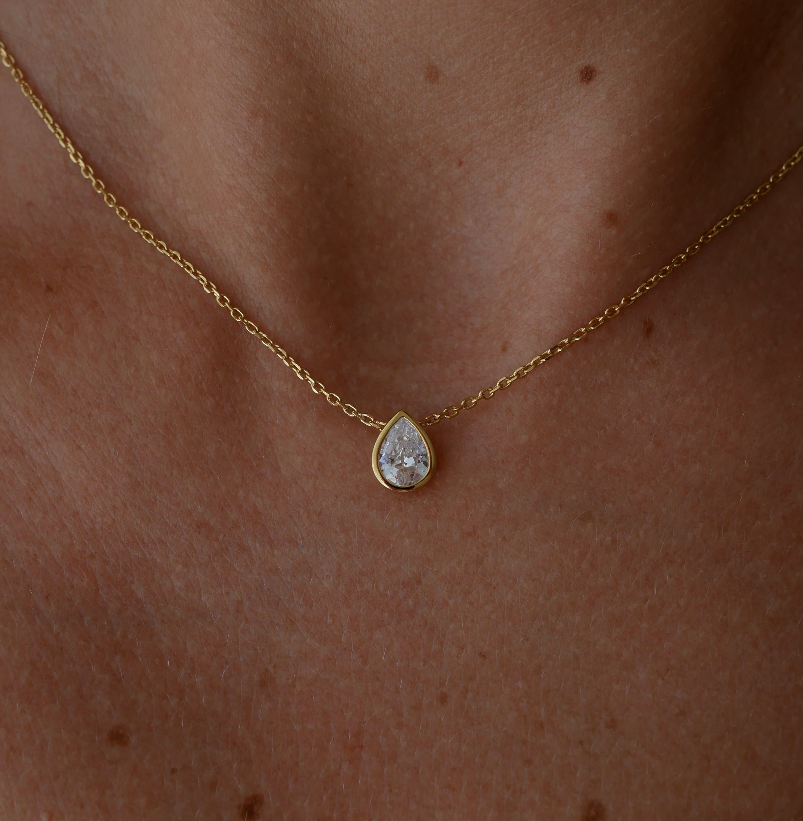 Gold necklace with a teardrop-shaped topaz pendant on a person's neck.