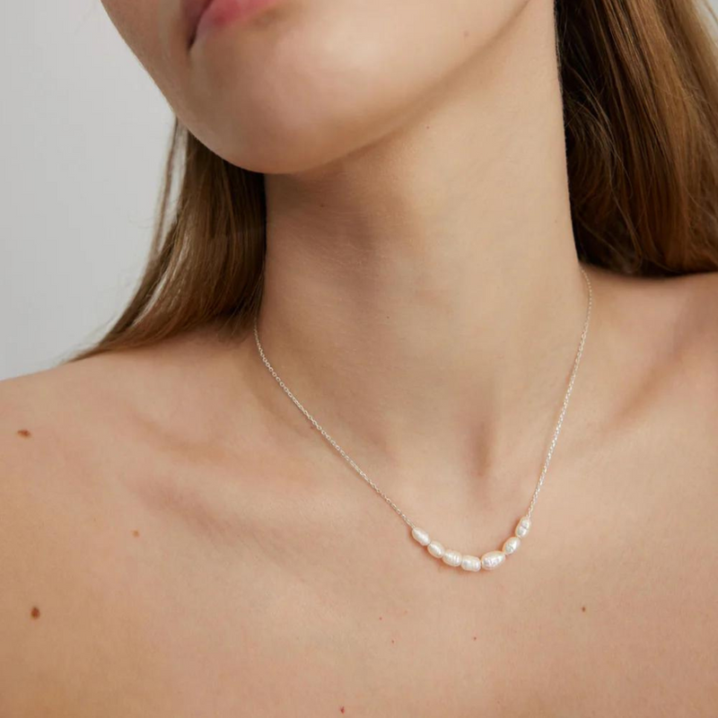 A silver necklace with river pearls displayed on a person's neck.
