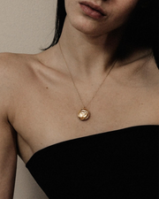 Woman wearing a gold necklace with a pendant against a neutral background