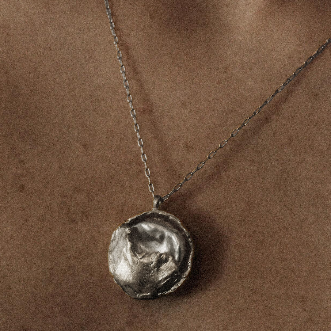 Silver necklace with a textured pendant on a brown background