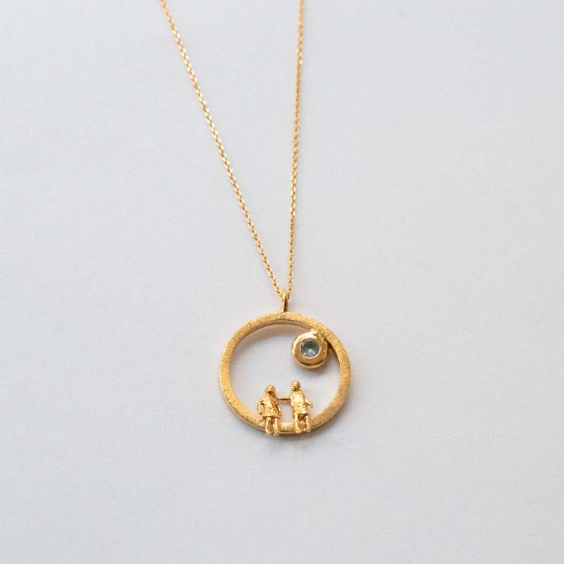 Gold necklace with a circular pendant featuring two figures and a gemstone on a light gray background