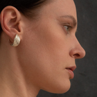 A close-up side profile of a woman wearing a textured, twisted silver hoop earring against a dark gray background.