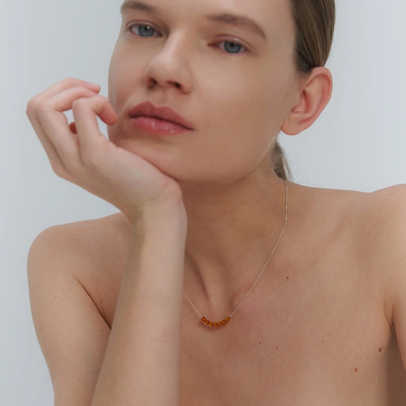 Woman wearing a silver necklace with Baltic amber beads against a plain background