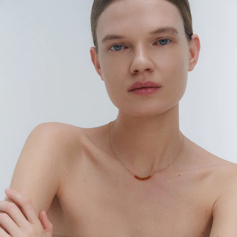 Woman wearing a gold necklace with Baltic amber beads against a plain background