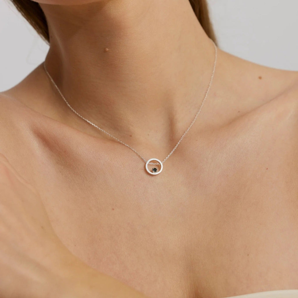 Necklace with a small round pendant on a person's neck against a neutral background