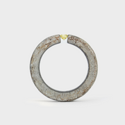 A hafnium ring with a grey patina and a yellow diamond set in a tension mount on the top, displayed against a white background.