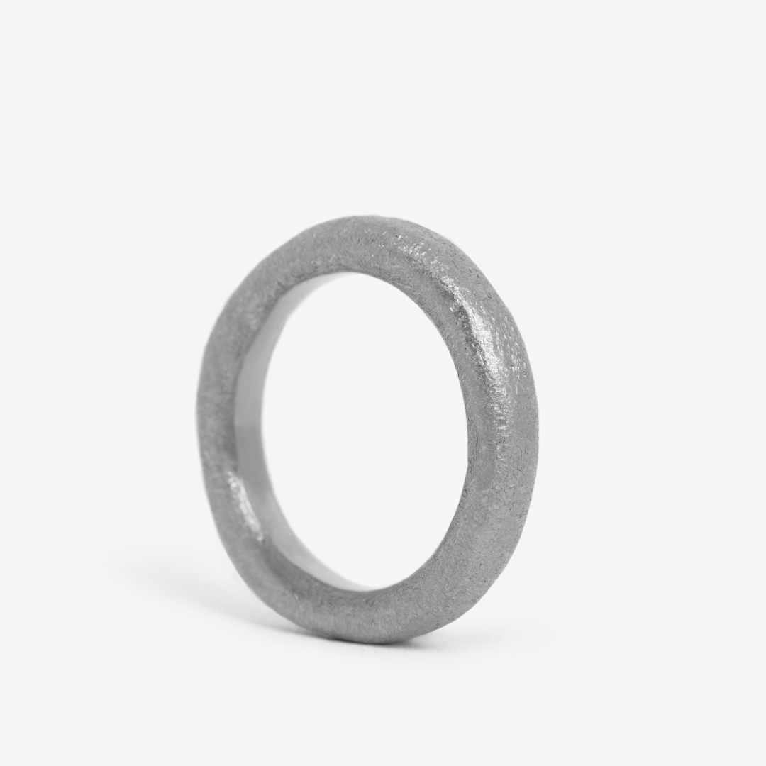 A single, hand-forged, 24k platinum ring with a textured surface, displayed on a white background.