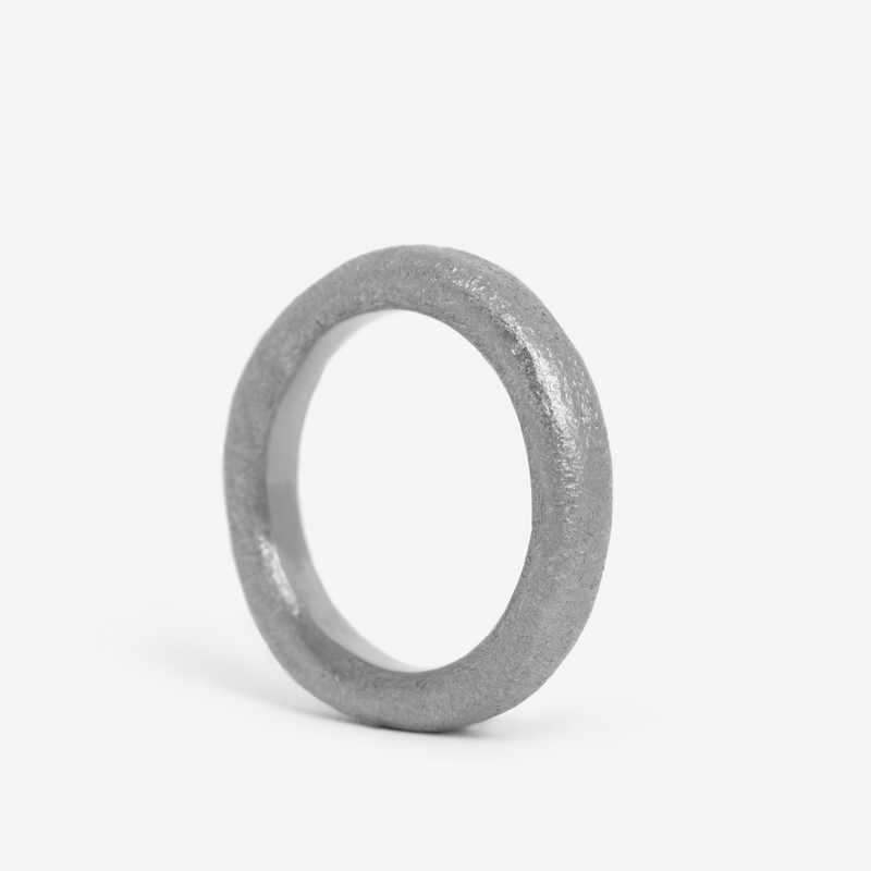A single, hand-forged, 24k platinum ring with a textured surface, displayed on a white background.