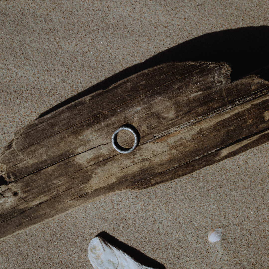 A single, hand-forged, 24k platinum ring with a textured surface, displayed on a wooden background.