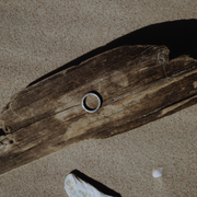 A single, hand-forged, 24k platinum ring with a textured surface, displayed on a wooden background.