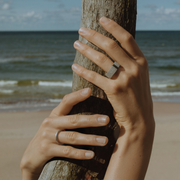 Hands wearing a single, hand-forged, 24k platinum ring with a textured surface.