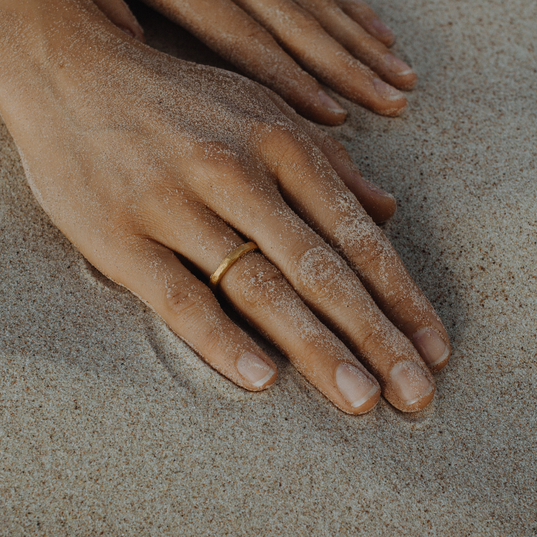 Hand wearing a single 24k gold hand-forged seamless ring on a white background
