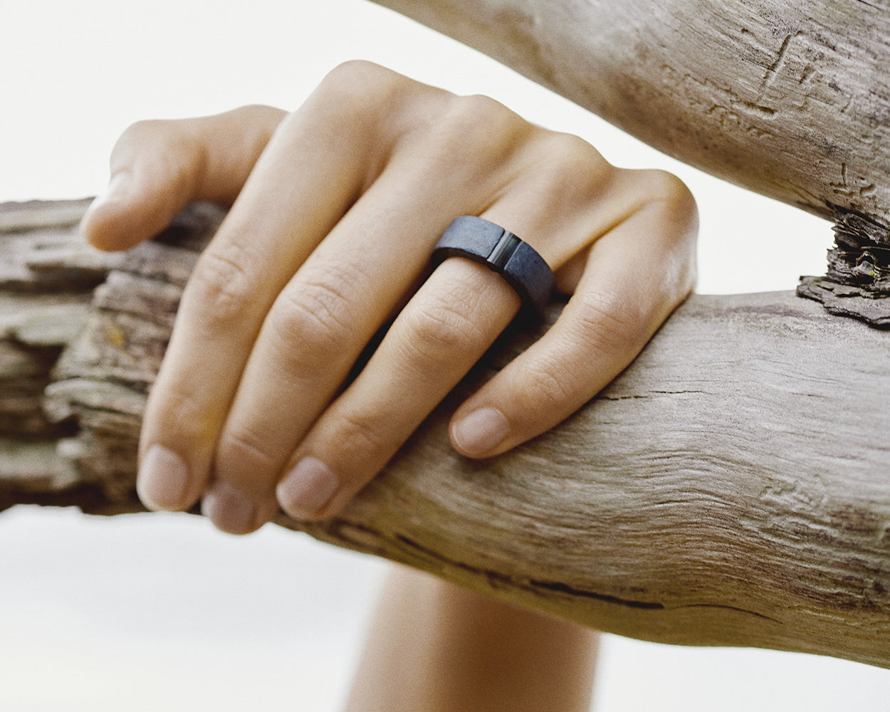 Hand with a ring on a finger against a blurred background. Ring is one-of-a-kind, composed of niobium and tourmaline.