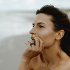 Woman with a ring on her finger against a blurred background. Ring is one-of-a-kind, composed of niobium and tourmaline.