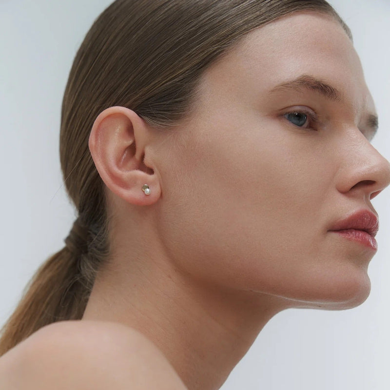 Close-up of a woman wearing minimal design yellow gold and freshwater pearl stud earrings by Adele Notes.