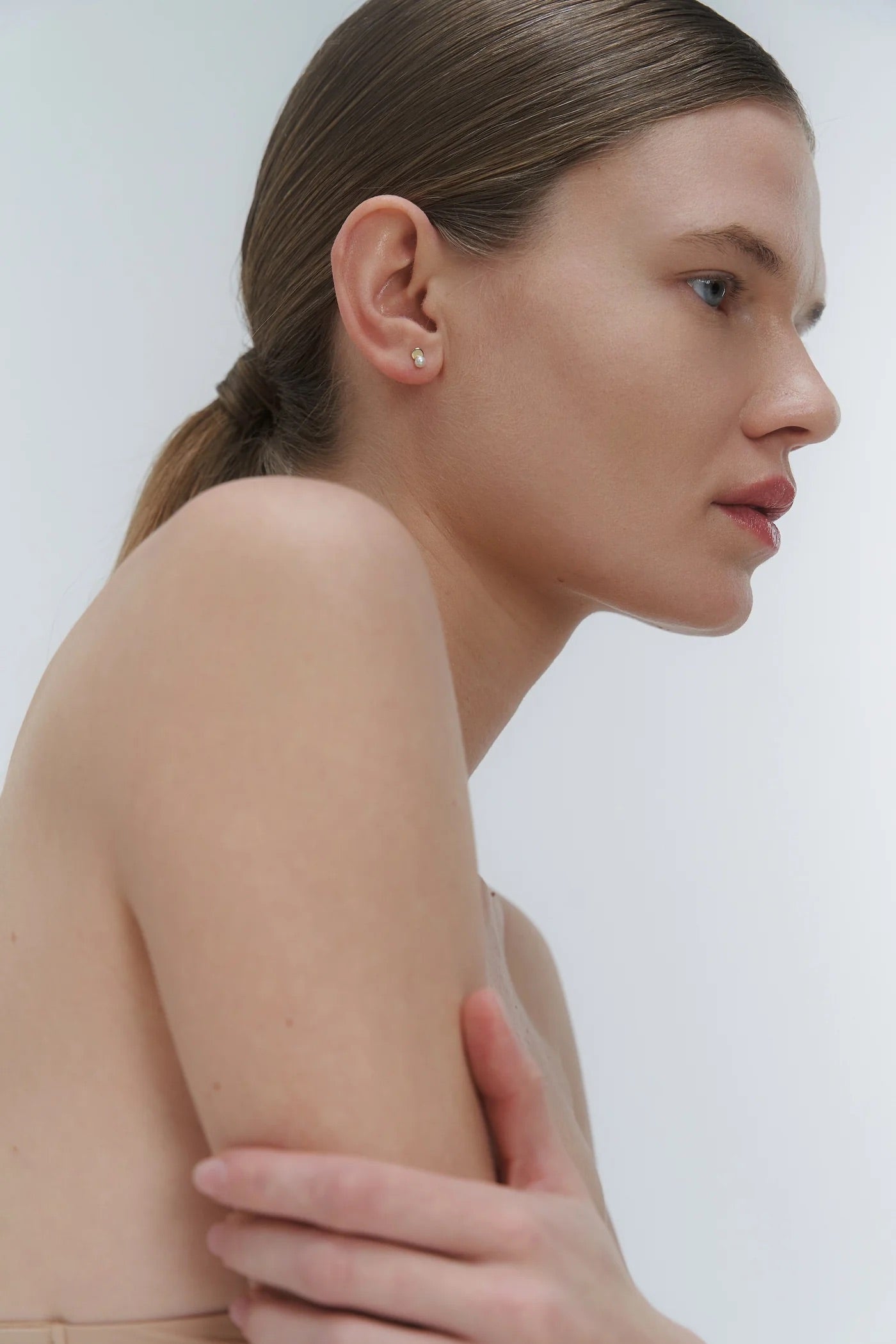 Woman with a ponytail and wearing minimal design yellow gold and freshwater pearl stud earring by Adele Notes.