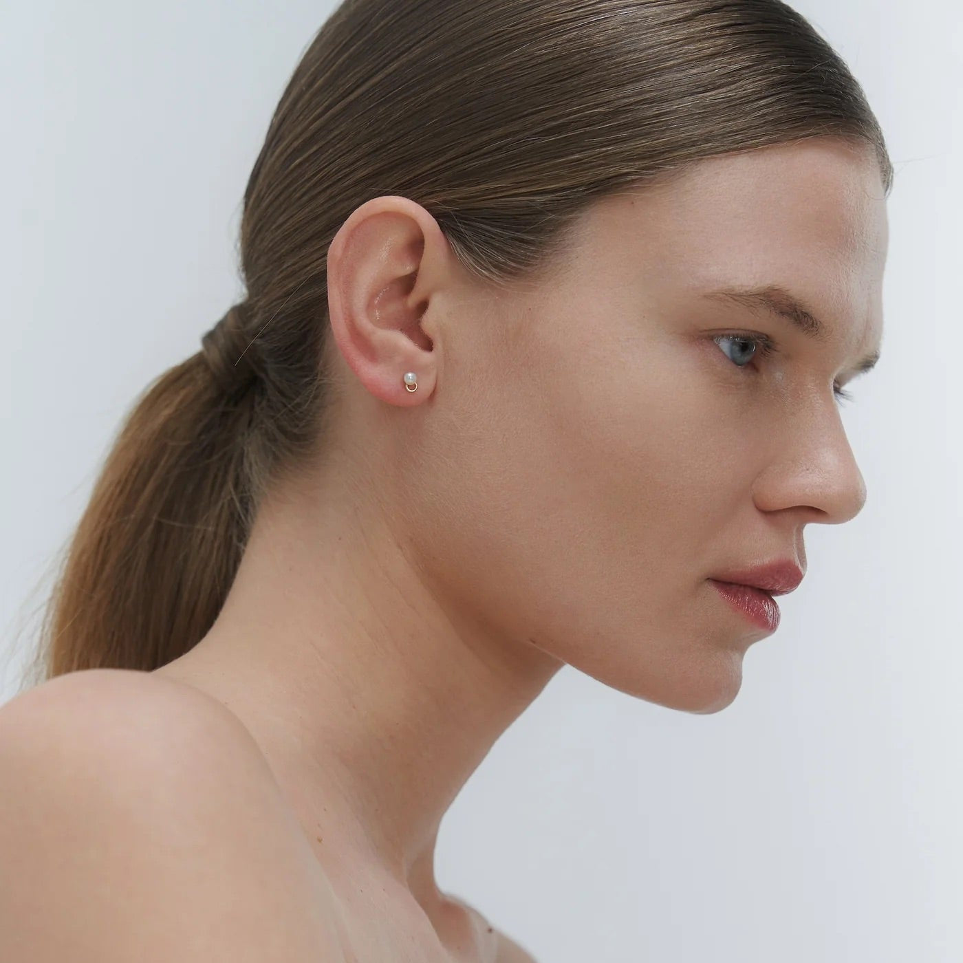 Woman wearing minimal design yellow gold and freshwater pearl stud earrings by Adele Notes
