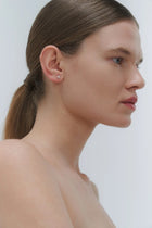 Woman wearing minimal design yellow gold and freshwater pearl stud earrings by Adele Notes