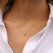 Yellow gold necklace with a small round diamonds pendant on a person wearing a white shirt.
