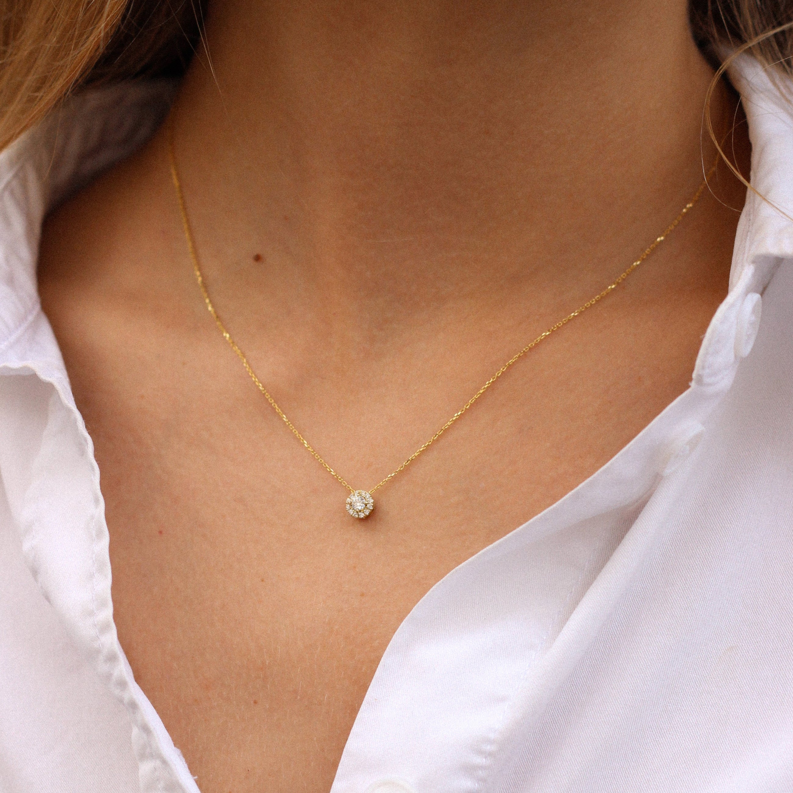 Yellow gold necklace with a small round diamonds pendant on a person wearing a white shirt.