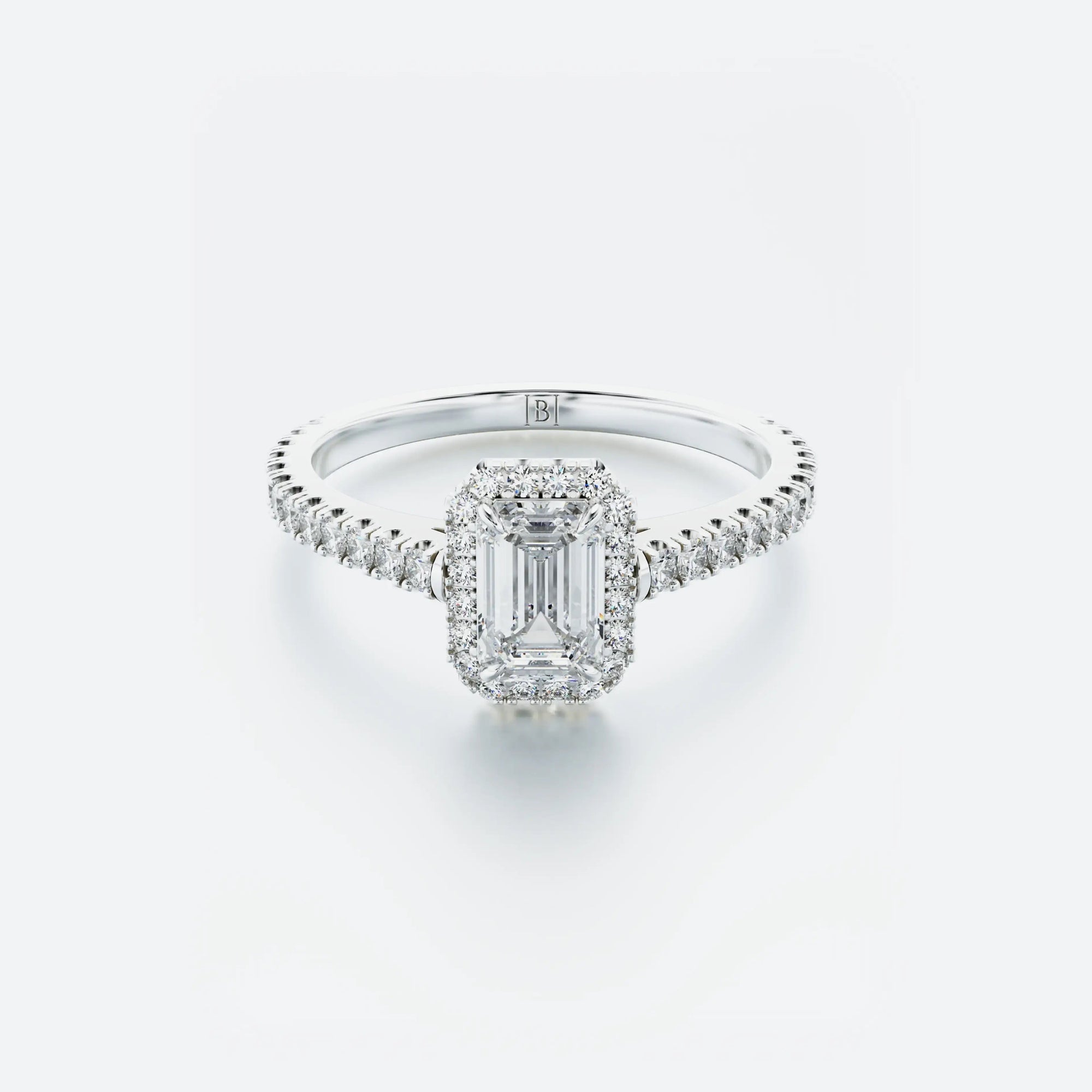 Diamond ring with emerald-cut center stone on a light gray background