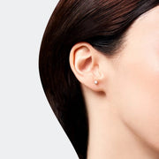 Close-up of an ear wearing a diamond stud earring on a plain background.
