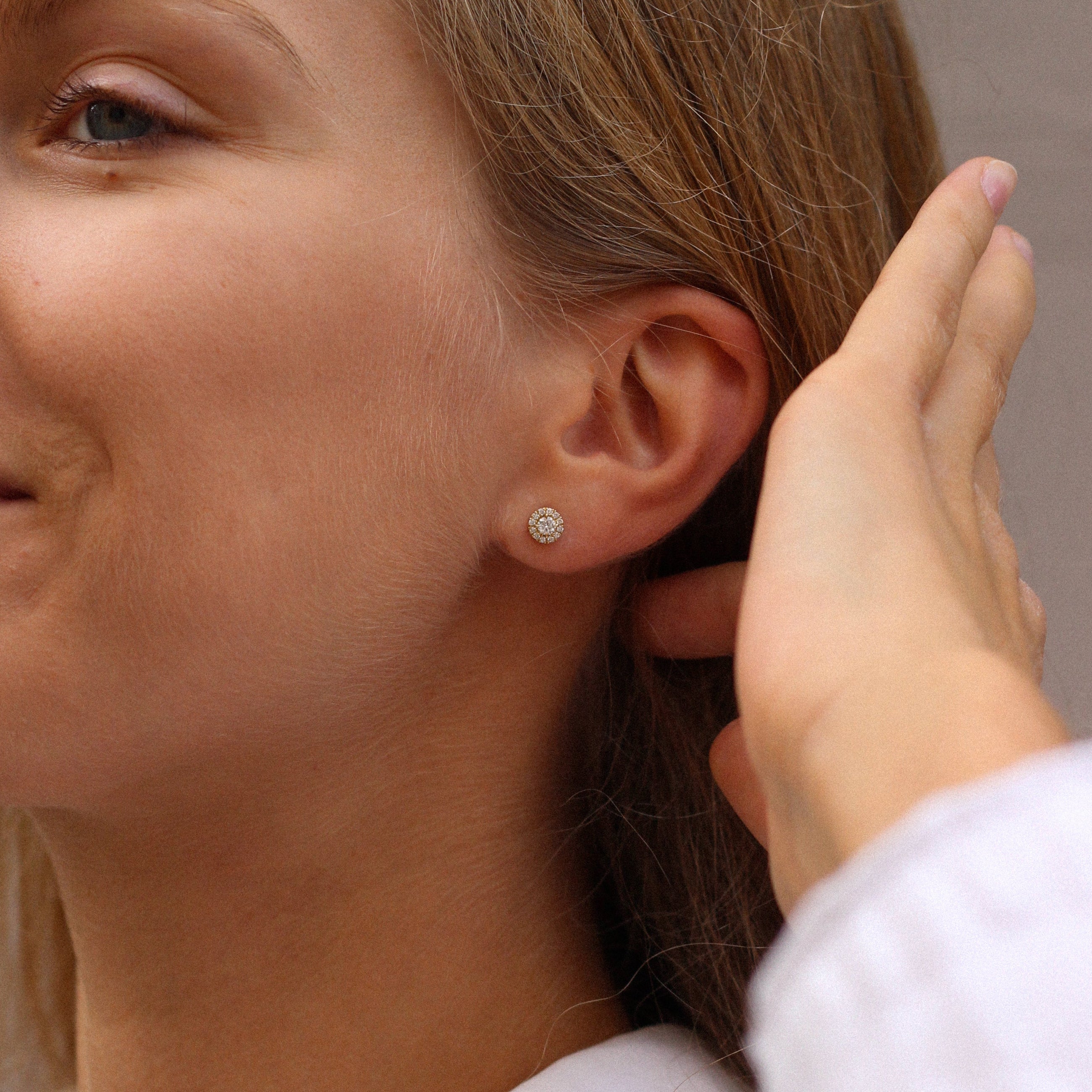 Woman wearing halo stud diamond earrings in 14k yellow gold featuring a central diamond surrounded by a delicate halo of pavé-set diamonds, with a total carat weight of 0.30 ct.
