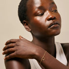 Woman wearing a gold bracelet with a heart design on a neutral background