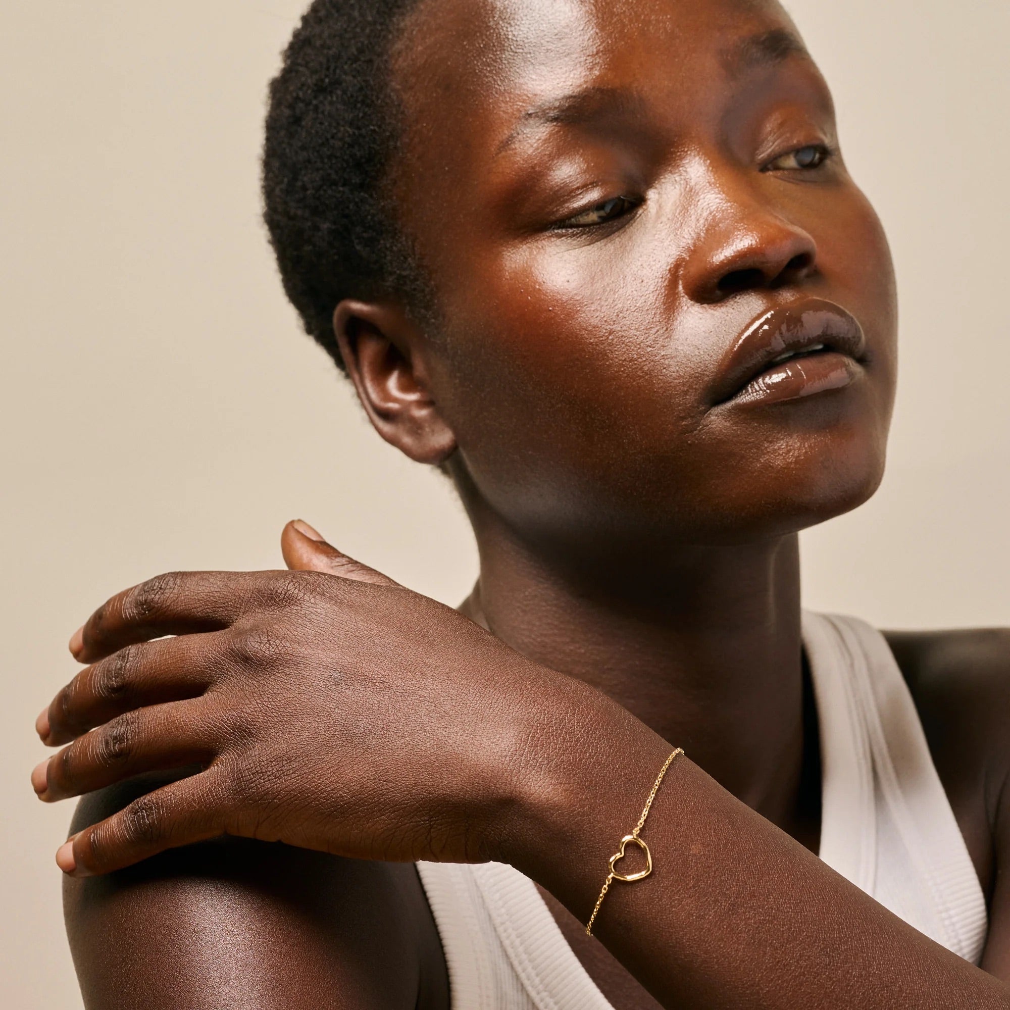 Woman wearing a gold bracelet with a heart design on a neutral background