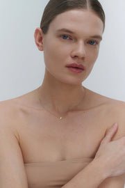Woman wearing a delicate gold necklace with cross pendant against a plain background
