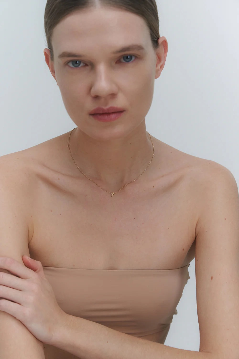 Woman wearing a delicate gold necklace with cross pendant against a plain background